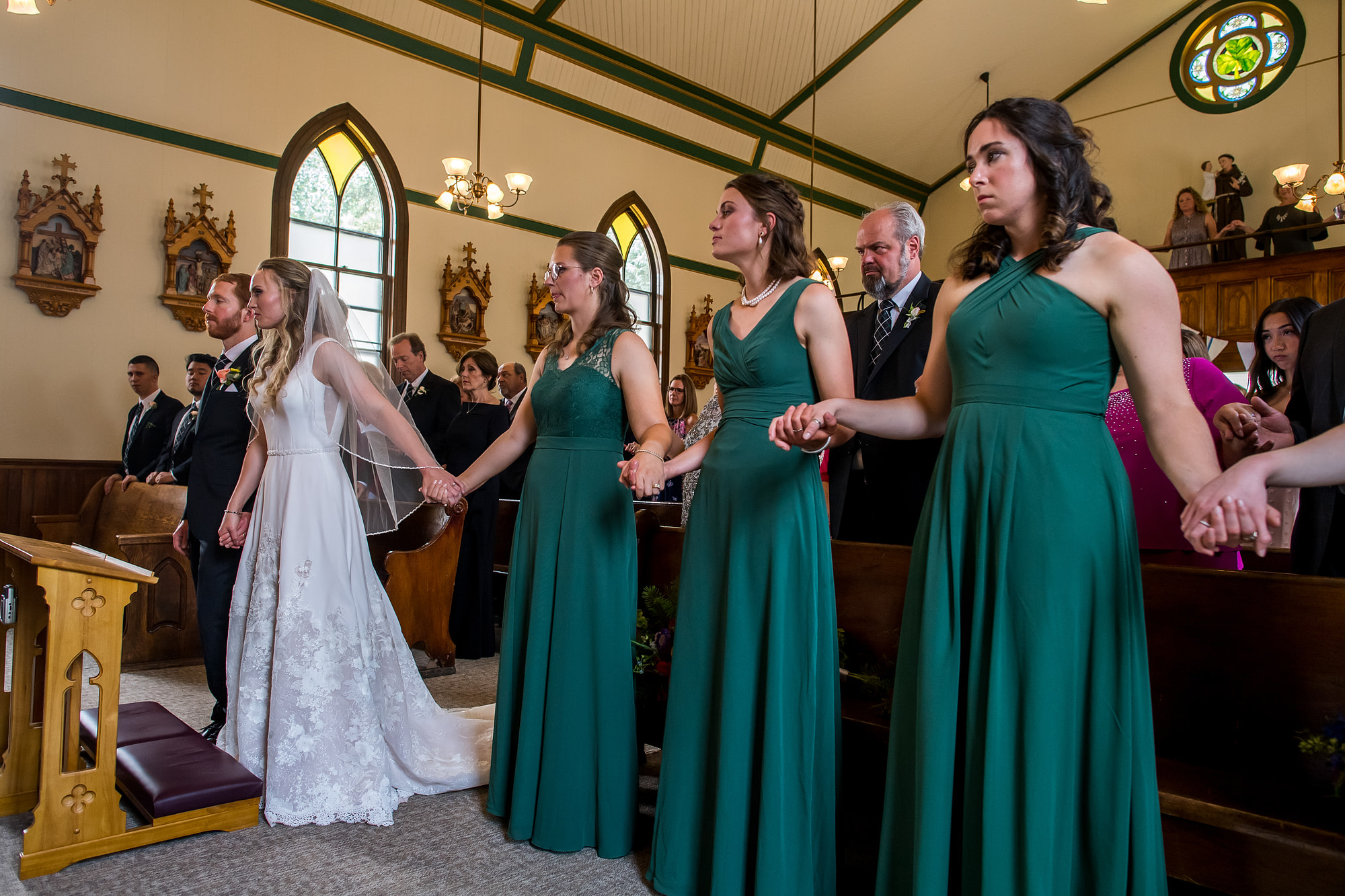 The bridesmaids and bride hold hands during the prayer of the faithful during a Telluride, Colorado, wedding at St. Patrick's Catholic Church.